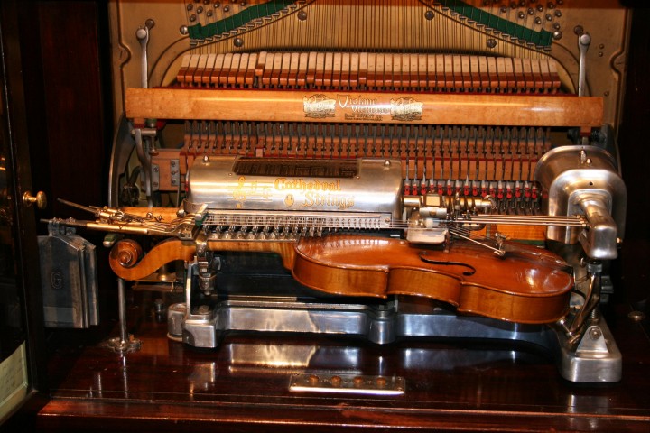 Picture showing a small string instrument clamped inside a mechanism reminiscent of the inside of a piano. Picture showing a small string instrument clamped inside a mechanism reminiscent of the inside of a piano.